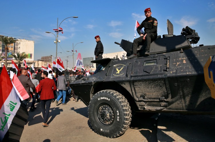 Security forces stand guard while supporters of Popular Mobilization Forces protest Sunday in Tahrir Square, Iraq. Thousands of Iraqis converged on a landmark central square in Baghdad on Sunday to commemorate the anniversary of the killing of Abu Mahdi al-Muhandis, deputy commander of the Popular Mobilization Forces, and General Qassem Soleimani, head of Iran's Quds force in a U.S. drone strike.