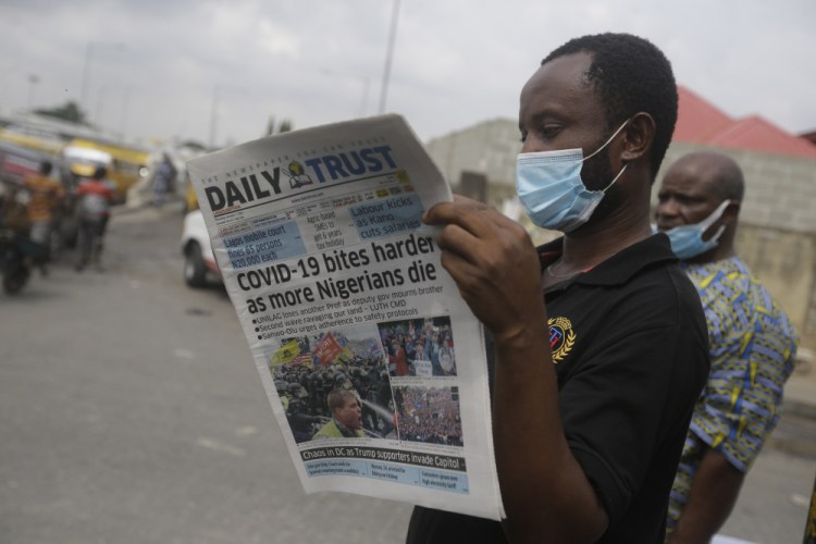 A man reads a newspaper reacting to the news of the assault on U.S Congress, on a street Thursday in Lagos, Nigeria. News reports show police with gun drawn as protesters try to break into the House Chamber at the U.S. Capitol on Wednesday in Washington.