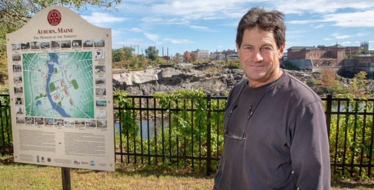 Peter Rubins from Grow L+A is a proponent of the twin cities assets, especially the Androscoggin river, stands on the Riverwalk in Auburn with a dry Great Falls in the background and one of the "Museum in the Streets"  signs that Lewiston will soon be erecting.