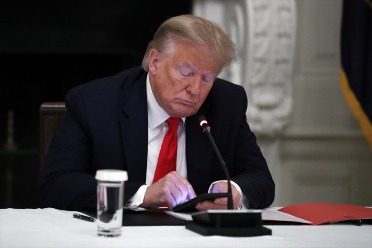 President Trump looks at his phone June 18 during a roundtable with governors on the reopening of America's small businesses, in the State Dining Room of the White House in Washington.