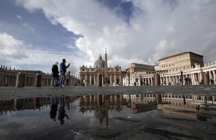 People are reflected on a puddle as they walk in an empty St.Peter's Square, as Pope Francis is reciting the Angelus noon prayer in his studio in the Apostolic palace, seen on the right, at the Vatican on Sunday. (AP Photo/Alessandra Tarantino)