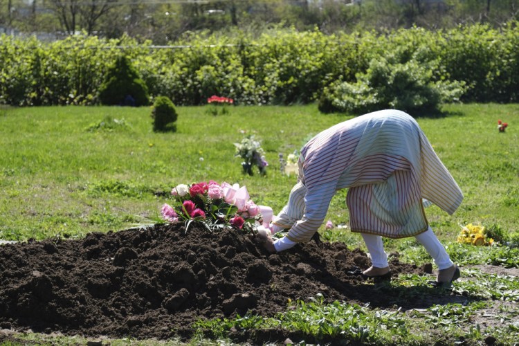 Erika Bermudez becomes emotional as she leans over the grave of her mother, Eudiana Smith, at Bayview Cemetery in Jersey City, N.J., on May 2. Bermudez was not allowed to approach the gravesite until cemetery workers had buried her mother, who died of COVID-19. Other members of the family and friends stayed in their cars. 