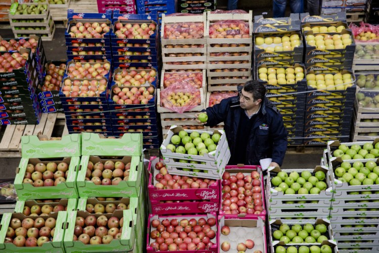 A buyer inspects a green apple as he stands beside crates of fresh produce in the fruit and vegetable section of Rungis wholesale food market in Rungis, France, on Jan. 15, 2015.