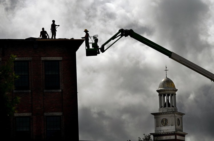 Workers work on the roof at the Lincoln Mill in Biddeford in September. The clock tower of Biddeford City Hall is to the right. A ground breaking ceremony took place in October of 2019 and when completed The Lincoln will be a mixed-use hotel and residential property located in the Lincoln Mill Building.