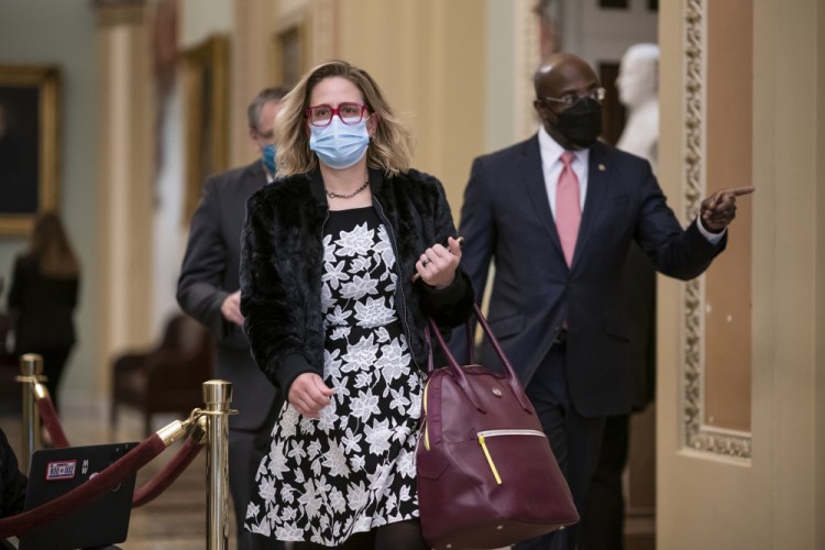 Sen. Kyrsten Sinema, D-Ariz., and Sen. Raphael Warnock, D-Ga., right, arrive as the second impeachment trial of former President Donald Trump starts in the Senate on Feb. 9. Sinema has suggested she may oppose boosting the federal minimum wage in the  relief package. 