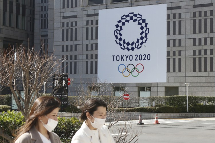 People wearing face masks pass by the logo of the Tokyo Olympics, in Tokyo, Wednesday, Feb. 17. The Olympics are scheduled to open on July 23 but recent polls show about 80% of the Japanese public want the Olympics canceled or postponed. 