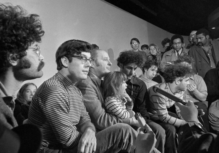 The defendants in the Chicago Seven trial hold a news conference in Chicago in 1970. Left to right, Lee Weiner, Rennie Davis, David Dellinger, Abbie Hoffman, Tom Hayden, (behind Hoffman), Jerry Rubin and John Froines. Dellinger holds his granddaughter, Michelle Burd. Davis has died at age 80. 