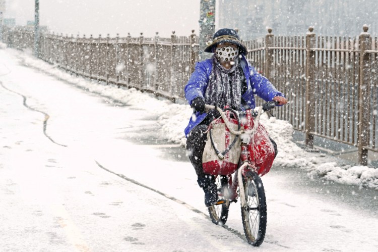 A woman rides a bicycle across the Brooklyn Bridge during Sunday's snow in the Brooklyn borough of New York. It was the second time in less than a week the area has been buffeted by heavy snowfall. (AP Photo/Kathy Willens)