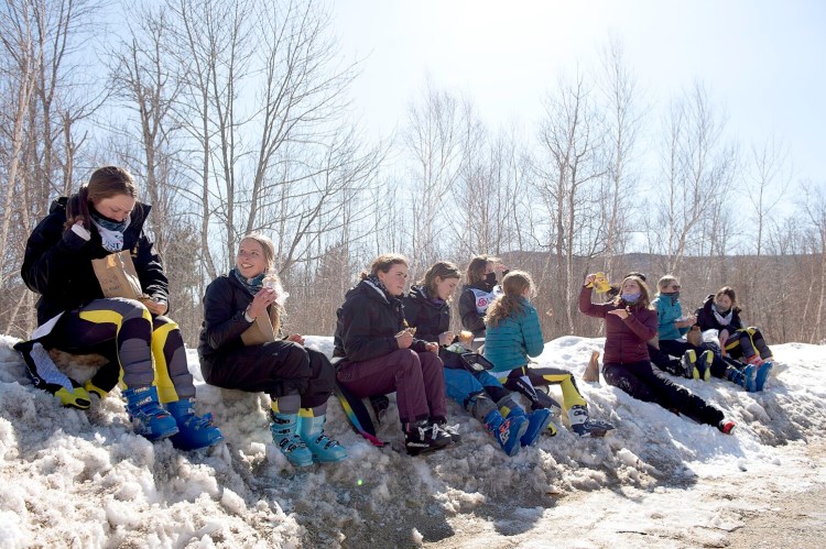 Members of the Maranacook High School women's alpine ski team eat lunch on a snowbank Thursday at Black Mountain in Rumford. Because of COVID-19 precautions, teams used their school bus as their ski lodge as the lodge was closed. Maranacook was one of eleven ski teams to compete during the KVAC Championships Thursday. The Maranacook team placed second behind Mount Blue High School.