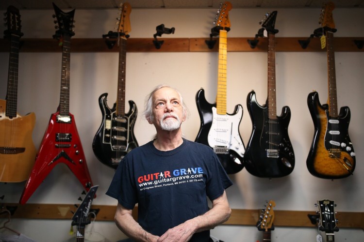Mike Fink, owner of Guitar Grave, stands next to his inventory of guitars at his South Portland shop on Monday. Fink says he's looking for a buyer, or a working partner, for the South Portland business after nearly 25 years of operation.