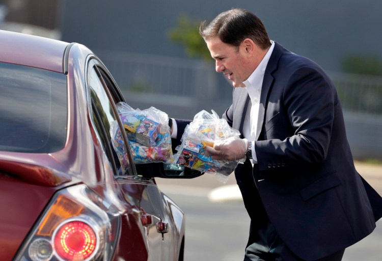 Arizona Gov. Doug Ducey serves meals to school children on March 19, 2020, outside Sunset Elementary School in Phoenix. Tuesday's announcement by the USDA will mean grab-and-go curbside offerings many families have relied upon during the crisis won't be disrupted and meals will be free for kids until Sept. 30. 