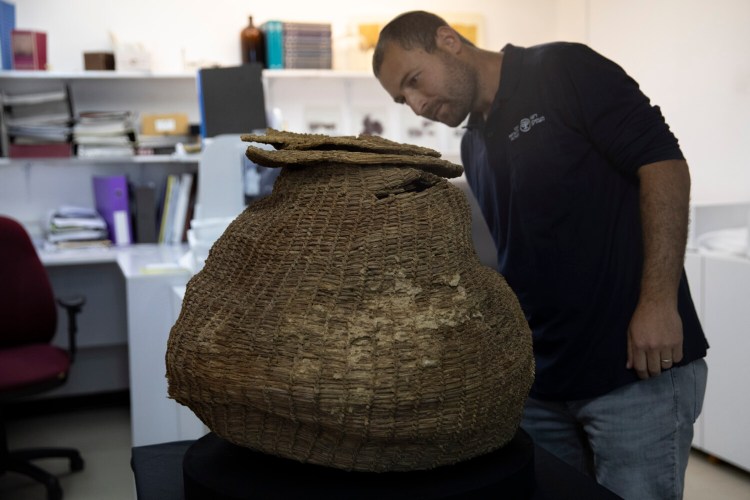 Archeologist Haim Cohen looks at a woven basket that was found during a sweep of more than 500 caves in the desert, at the Israeli Antiquities Authority Dead Sea scrolls conservation lab in Jerusalem, Tuesday, March 16, 2021. Israeli archaeologists on Tuesday announced the discovery of dozens of new Dead Sea Scroll fragments bearing a biblical text found in a desert cave and believed hidden during a Jewish revolt against Rome nearly 1,900 years ago. Alongside the Roman-era artifacts, items shown to journalists Tuesday included far older discoveries including the immense, complete woven basket from the Neolithic period, estimated to be 10,500 years old, preserved in caves' arid climate. (AP Photo/Sebastian Scheiner)