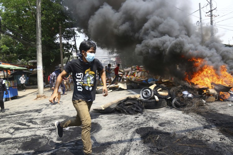 Anti-coup protesters run around their makeshift barricade they burn to make a defense line during a demonstration Sunday in Yangon, Myanmar.