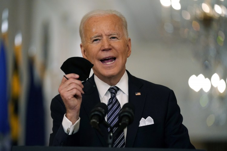 President Joe Biden holds up his face mask as he speaks about the COVID-19 pandemic during a prime-time address from the East Room of the White House on Thursday in Washington. 
