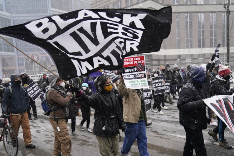 A group of protesters march in the snow around the Hennepin County Government Center on Monday in Minneapolis, where the second week of jury selection continues in the trial for former Minneapolis police officer Derek Chauvin. Chauvin is charged with murder in the death of George Floyd during an arrest last may in Minneapolis.