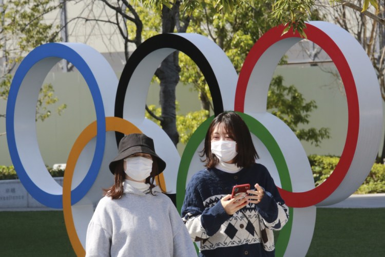 People walk past the Olympic rings in Tokyo on March 17. The Tokyo Olympics open in under four months, and the torch relay has begun to crisscross Japan with 10,000 runners. Organizers say they are mitigating the risks, but many medial expert aren't convinced.