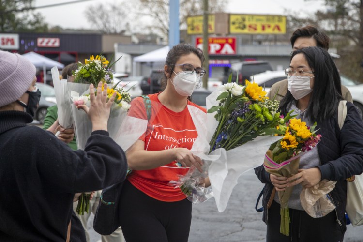 Roula AbiSamra, center, and Chelsey, right, prepare to lay flowers bouquets at a makeshift memorial outside of the Gold Spa in Atlanta. 