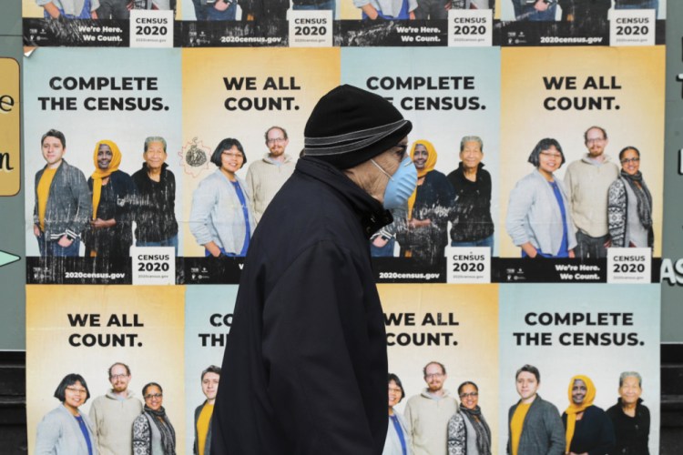 A man wearing a mask walks past posters encouraging participation in the 2020 Census April 1, 2020, in Seattle's Capitol Hill neighborhood.