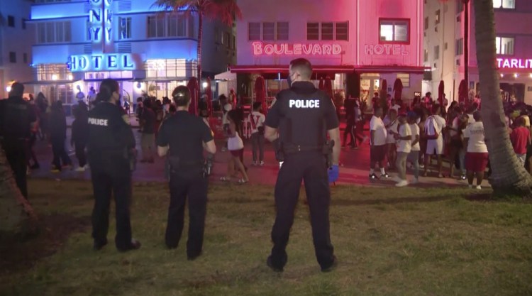 Police officers stand guard Saturday evening, as crowds descend on South Beach in Miami.  After days of partying and confrontations between police and large crowds, Miami Beach officials have ordered an emergency curfew. 