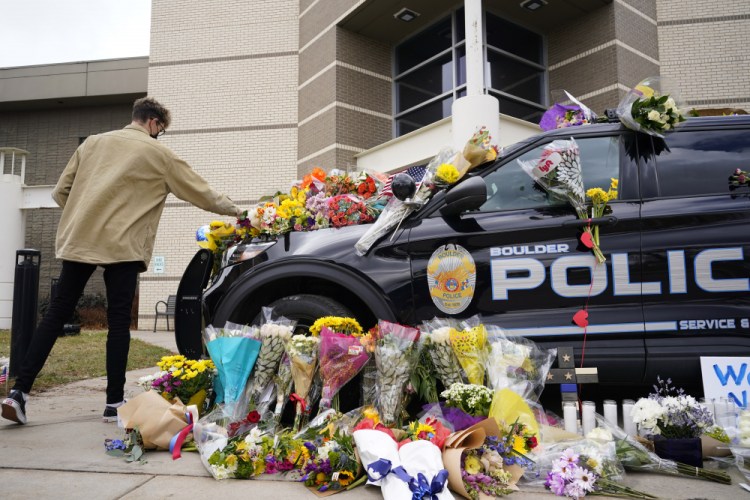 A man leaves a bouquet on a police cruiser parked outside the Boulder Police Department after an officer was one of the victims of a mass shooting at a King Soopers grocery store, on Tuesday in Boulder, Colo. 