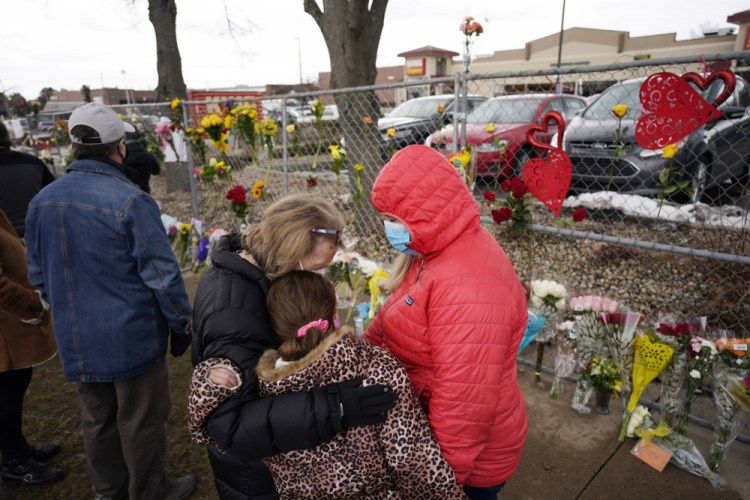 Mourners embrace after leaving bouquets on a fence put up around the parking lot where a mass shooting took place in a King Soopers grocery store, on Tuesday in Boulder, Colo. 