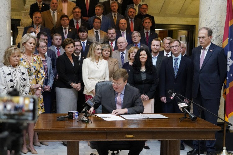 Mississippi Gov. Tate Reeves signs the first state bill in the U.S. this year to ban transgender athletes from competing on female sports teams, as supporting lawmakers gather behind him, Thursday at the Capitol in Jackson, Miss.
