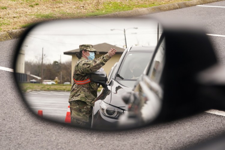 A National Guard soldier directing drivers is reflected in the mirror of a car waiting in a COVID-19 vaccination line Feb. 26 in Shelbyville, Tenn. Tennessee has continued to divvy up vaccine doses based primarily on how many people live in each county, and not on how many residents belong to eligible groups within those counties. 