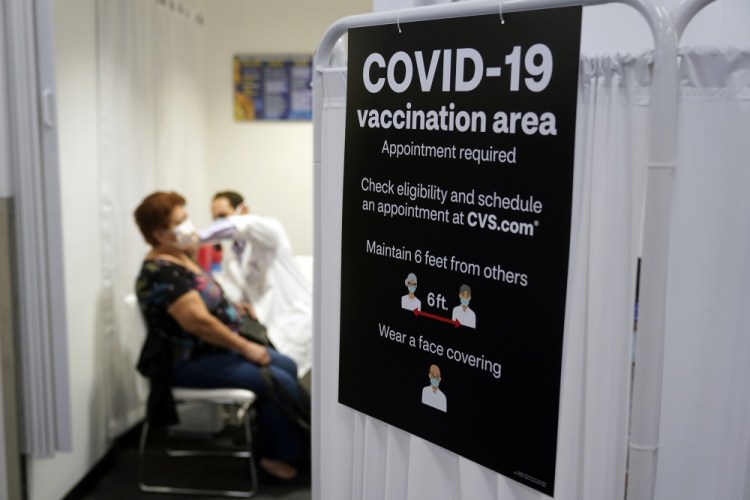 A patient receives a shot of the Moderna COVID-19 vaccine next to a guidelines sign at a CVS Pharmacy branch in Los Angeles on Monday. More than 28 million Americans fully vaccinated against the coronavirus will have to keep waiting for guidance from U.S. health officials for what they should and shouldn’t do. 