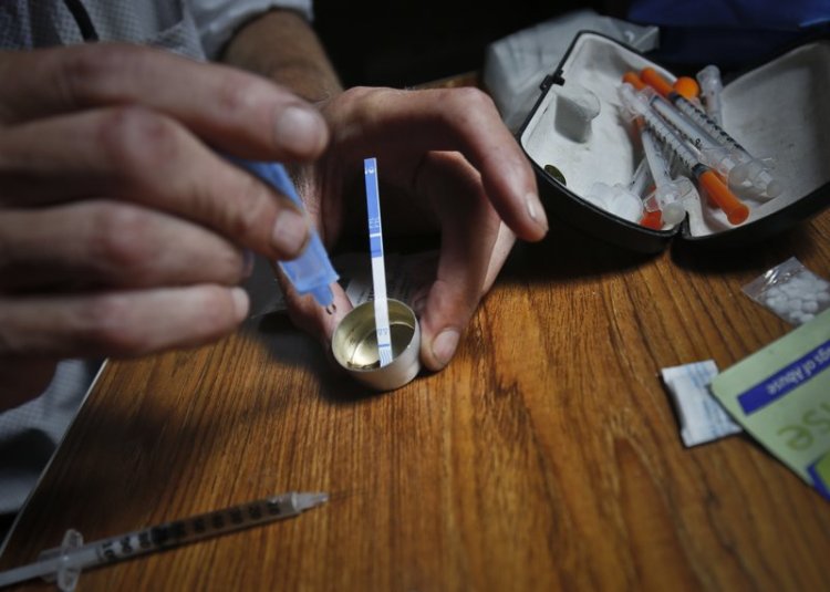 An unidentified man preparing to inject heroin adds some of the diluted drug to a mixing container in this photo taken in New York in 2018. A blue and white fentanyl test strip inserted into the mixing container will indicate whether it contains fentanyl. 