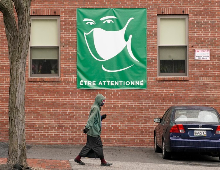 PORTLAND, ME - APRIL 5: A woman walks along State Street in Portland on Monday, April 5, 2021 underneath a sign of a person wearing a mask with a French phrase that translates loosely to “be attentive.” (Staff photo by Gregory Rec/Staff Photographer)