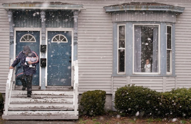 BIDDEFORD, ME - APRIL 16: As a combination of sleet and snow fall, a girl looks out from a window as Matt Gauthier, a city carrier with the U.S. Postal Service, walks down stairs after delivering mail to a house on Graham Street in Biddeford on Friday, April 16, 2021. (Staff photo by Gregory Rec/Staff Photographer)