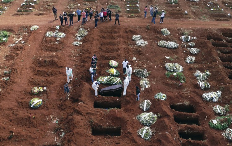 Cemetery workers wearing protective gear lower the coffin of a person who died from complications related to COVID-19 into a gravesite at the Vila Formosa cemetery Wednesday in Sao Paulo, Brazil. 