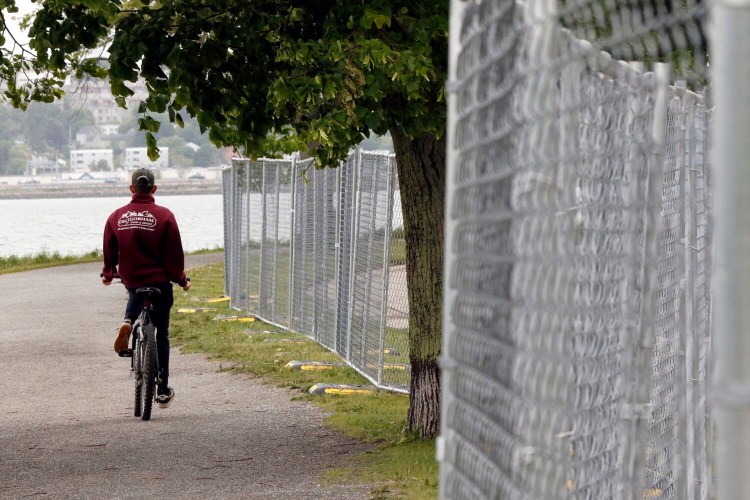 A cyclist rides on the Back Cove Trail alongside Baxter Boulevard near the intersection of Dartmouth Street in Portland on Saturday. The city has installed fencing around Back Cove as part of a new sewer separation project.