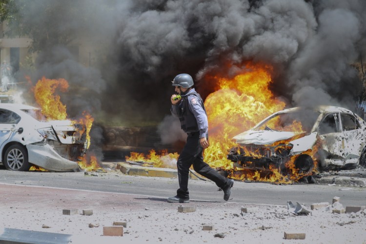 An Israeli firefighter walks next to cars hit by a missile fired from Gaza Strip, in the southern Israeli town of Ashkelon, Tuesday, May 11. 