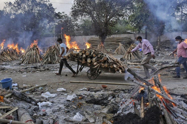 A worker carries wood on a hand cart as funeral pyres of COVID-19 victims burn at a crematorium on the outskirts of New Delhi, India, on Saturday.