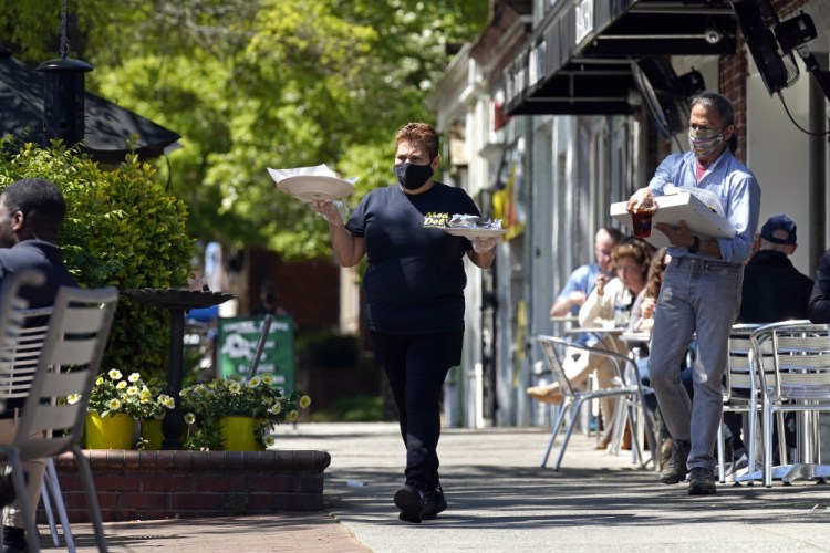 A member of the wait staff takes food to outdoor diners at the Mediterranean Deli restaurant in Chapel Hill, N.C., Friday, April 16. Thousands of restaurants and bars decimated by COVID-19 have a better chance at survival as the government begins handing out $28.6 billion in grants.