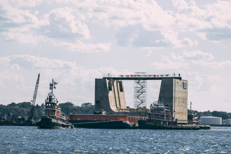 In this photo provided by Cianbro Corp., a 5,000-ton concrete entrance structure is towed out of the harbor, Sunday, June 20, 2021, in Portland, Maine. The structure, built by Cianbro in Portland, will be used by the Navy at the "Superflood Basin" project at the Portsmouth Naval Shipyard, in Kittery, Maine. The structure will allow submarines easier access to dry docks. (Cianbro Corp. via AP)