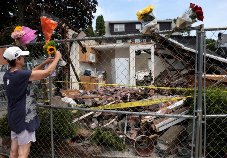 In this Sunday, June 27, 2021 photo, a neighbor places a bouquet of flowers on a fence outside of a building in Winthrop, Mass., where an armed man crashed a hijacked truck on Saturday, then fatally shot two bystanders before being killed by police. (Jessica Rinaldi/The Boston Globe via AP)