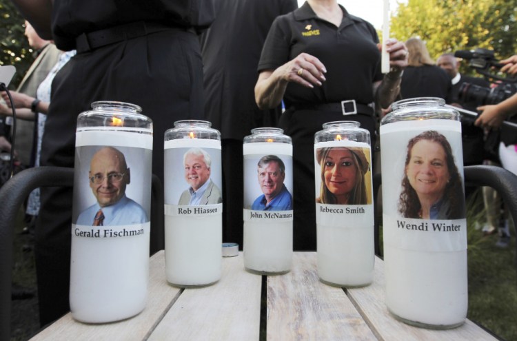 In this June 29, 2018, file photo, photos of five employees of the Capital Gazette newspaper adorn candles during a vigil across the street from where they were slain in the newsroom in Annapolis, Md. 