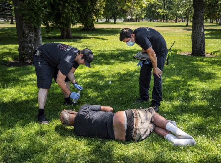 With the temperature well over 100 degrees, Spokane, Wash., firefighter Sean Condon, left, and Lt. Gabe Mills, assigned to the Alternative Response Unit of of Station 1, check on the welfare of a man in Mission Park in Spokane on Tuesday. The special fire unit, which responds to low-priority calls, has been scrambling during this week's heat wave.