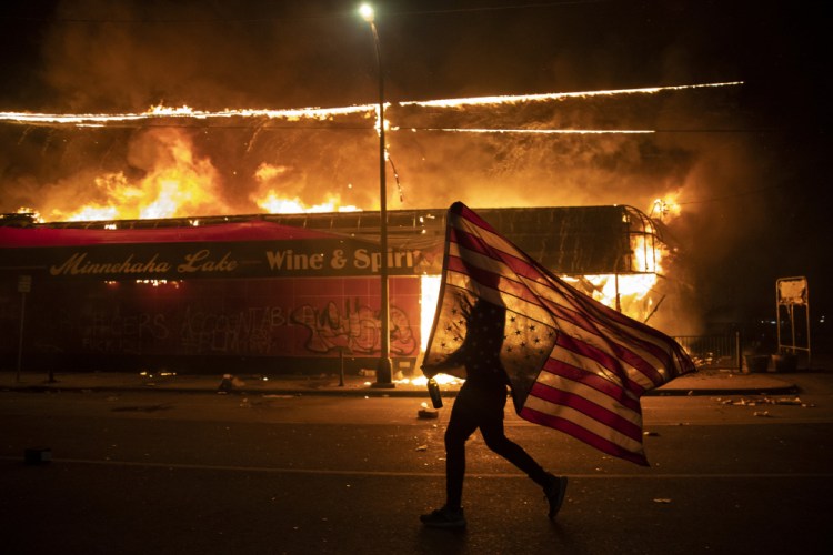 A protester carries a U.S. flag upside down, a sign of distress, next to a burning building, May 28, 2020, in Minneapolis. The image was part of a series of photographs by The Associated Press that won the 2021 Pulitzer Prize for breaking news photography. 