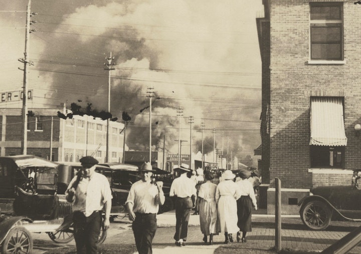Two armed men walk away from burning buildings during the Tulsa Race Massacre in 1921.