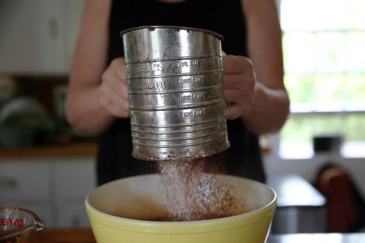 BRUNSWICK, ME - JULY 29: Christine Burns Rudalevige sifts flour, cocoa powder, baking powder, cinnamon and baking soda into a mixture of sugar, oil, vanilla, whole eggs and extra yolk, buttermilk, coffee and salt for folding. (Staff photo by Ben McCanna/Staff Photographer)