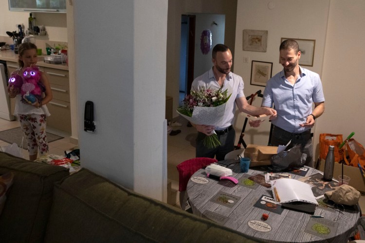 Etai, right, and Yoav Pinkas-Arad read a card that arrived with flowers as their daughter Or watches, in their house in Tel Aviv, Israel, Sunday, July 11, 2021.  Israel’s Supreme Court on Sunday cleared the way for same-sex couples to have children through surrogate mothers, a move hailed by lawmakers and activists as a victory for LGBTQ rights. Etai and Yoav, a gay couple had appealed to the court against the surrogacy law in 2010. (AP Photo/Sebastian Scheiner)
