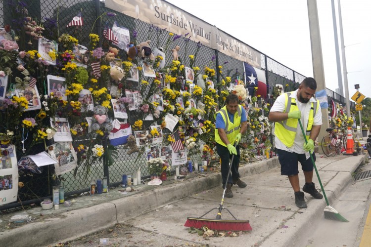 Workers with Surfside Public Works sweep up dead flowers from a makeshift memorial for victims of the collapsed Champlain Towers South condominium building  Tuesday in Surfside, Fla. 

