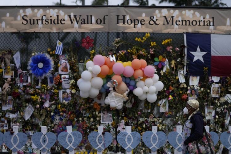 A woman walks past a makeshift memorial for the victims of the Champlain Towers South building collapse, on Monday, July 12, in Surfside, Fla.