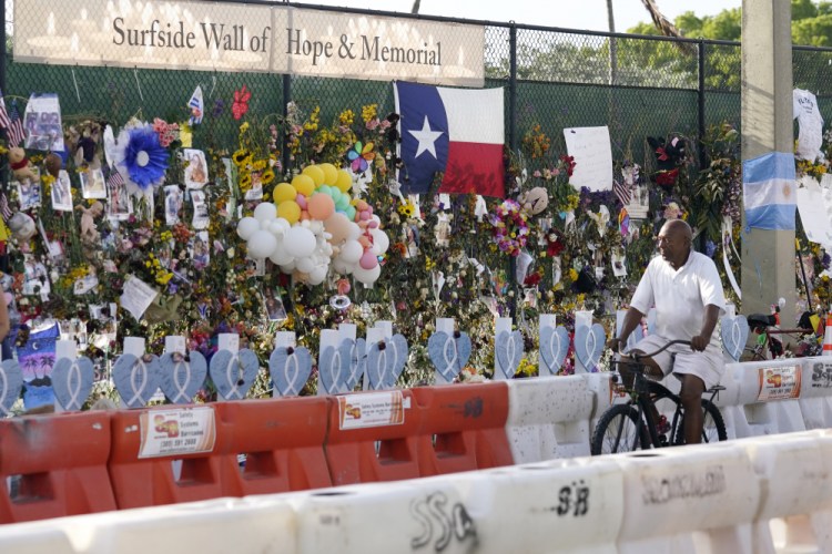A cyclist rides past a makeshift memorial recognizing the victims of the partially collapsed Champlain Towers South building, as removal and recovery work continues at the site, Tuesday, July 13, in Surfside, Fla. 