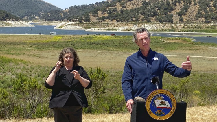 Gov. Gavin Newsom and interpreter Julia Townsend stand at the edge of a diminished Lopez Lake near Arroyo Grande, Calif., on Thursday.

