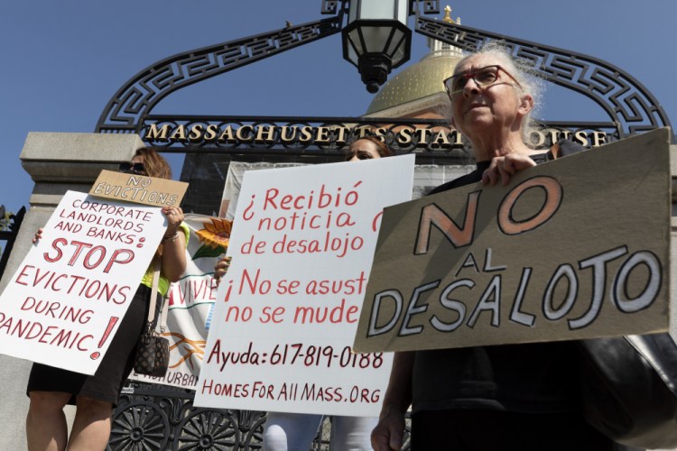 People from a coalition of housing justice groups hold signs protesting evictions during a news conference outside the Statehouse on Friday,  in Boston.