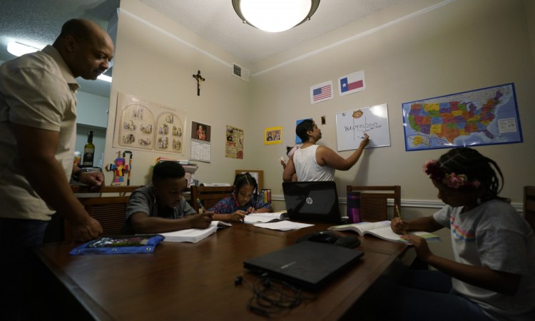 Arlena Brown, center, holds her youngest child, Lucy, 9 months, as she and husband, Robert, left, lead their other children, from left, Jacoby, 11; Felicity, 9, and Riley, 10, through math practice Tuesday at their home in Austin, Texas. “I didn’t want my kids to become a statistic and not meet their full potential,” said Robert, a former teacher who now does consulting. “And we wanted them to have very solid understanding of their faith.”